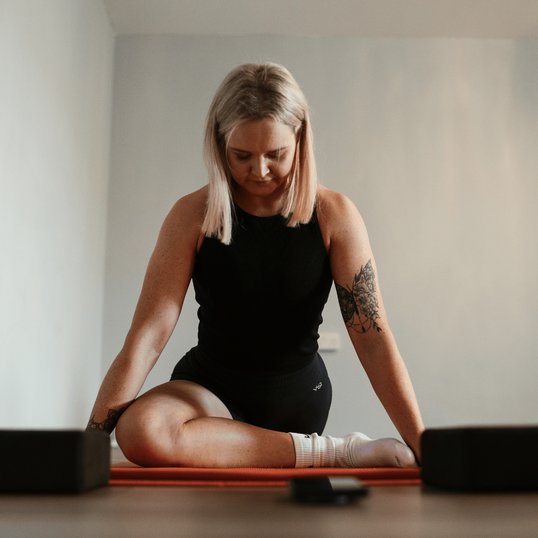 Anita pictured doing pigeon stretch on yoga mat with two yoga blocks either side