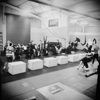 Team Workout-multiple clients doing box jumps, using assault bike & rower machines in the gym